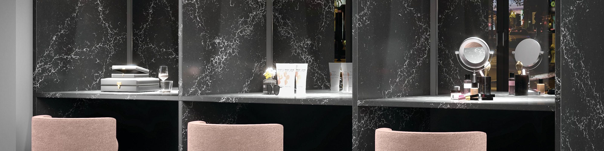 Dressing room with pink vanity stools in front of makeup mirrors divided by black & white quartz walls that look like marble.
