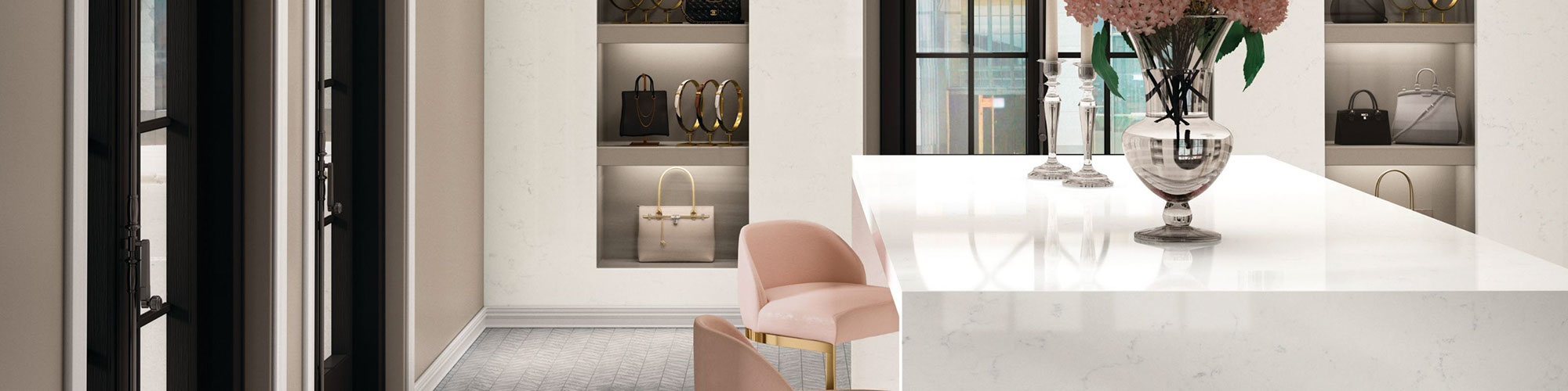 Boutique with white quartz waterfall countertop, pink & brass chairs, gray chevron mosaic floor tile, white quartz seamless wall with open shelves holding handbags.