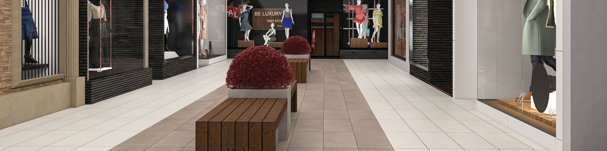 Shopping mall with brown and beige floor tile that looks like concrete, wood benches around concrete planters, and store windows with mannequins in women’s clothing.
