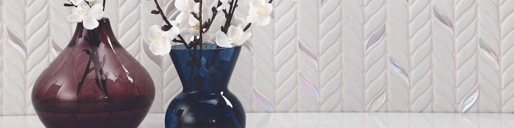 Closeup of textured wall with white leaf-shaped mosaic tile, blue and maroon vases holding white flowers.