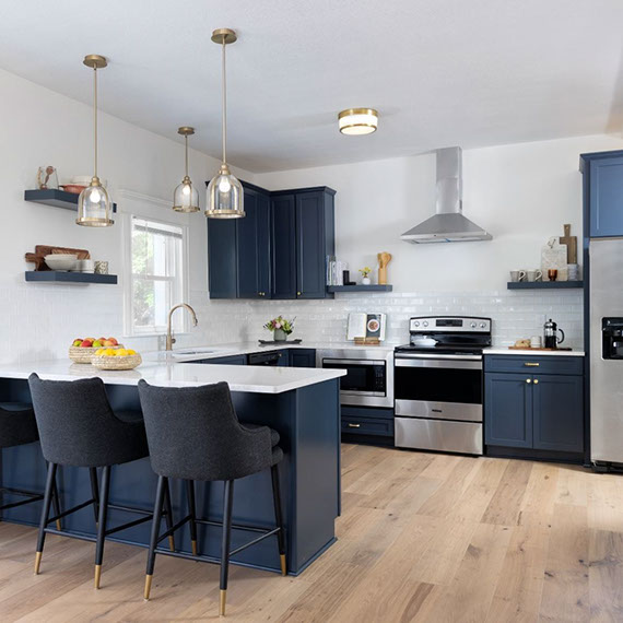 Renovated kitchen with navy cabinets and floating shelves, white glossy subway tile backsplash, white quartz countertops, and stainless steel appliances.