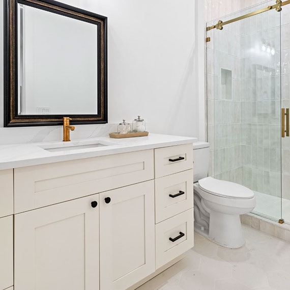 Renovated bathroom with white quartz countertops, off-white cabinets, off-white glossy shower wall tile, and off-white hexagon floor tile.