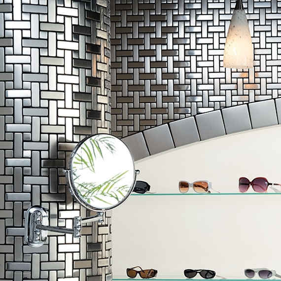 Sunglass store with brushed steel mosaic wall tile with inset glass shelves trimmed with 4x4 metal tile, holding sunglasses.