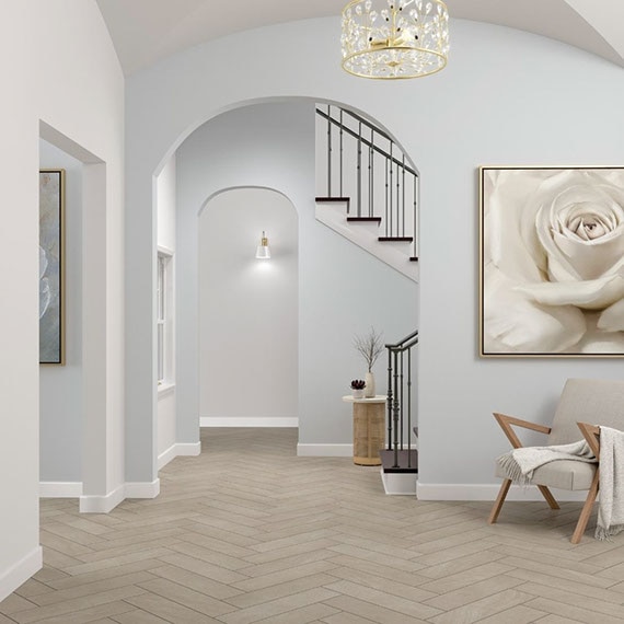 Foyer with arched doorways, gray floor tile that looks like stone set in a herringbone pattern, wood chair with off-white cushions.