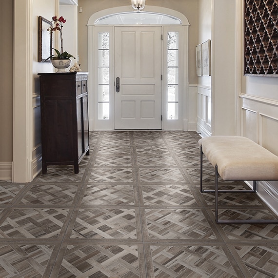 Residential foyer with floor tile that looks like wood in a cassettone pattern, white door with side windows, pendant lighting, and coffered ceiling.