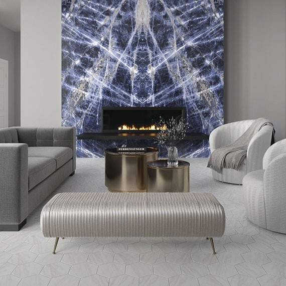 Modern living room with fireplace surround of dark blue bookmatched slab with white striations, beige & white marble look hexagon floor tile, and gray velvet sofa.