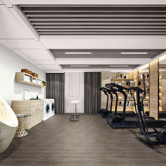 Home gym with floor tile that looks like dark wood, 2 treadmills, elliptical machine, front-loading washer and dryer, sink with wood cabinets, and floating shelves.