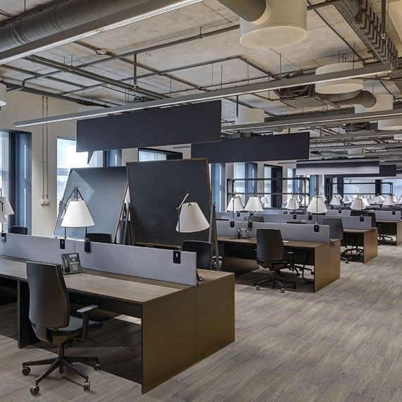 Industrial décor open office design with floor tile that looks like wood flooring, wood desks with rolling chairs, ceiling with expose pipes and air conditioner vents.