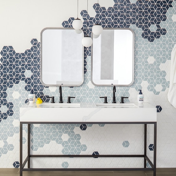 Bathroom with light blue, navy & and white cube mosaic tile backsplash and white porcelain slab countertop on double-sink vanity with black metal legs.