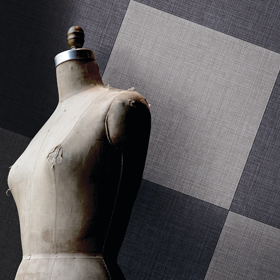 Navy and light gray fabric look tile in a checkered pattern on the wall behind well-worn sewing mannequin.