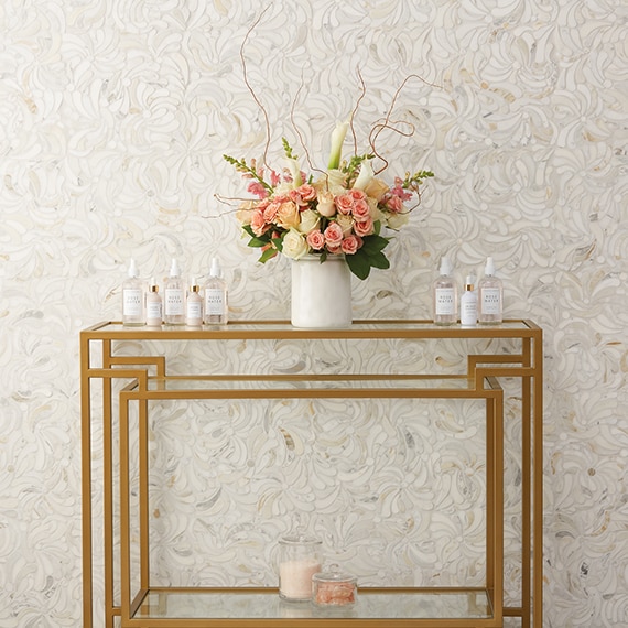 Closeup of white, gray, and beige marble mosaic wall tile and brass cart with glass top, pink & white bouquet of flowers in a white vase. 