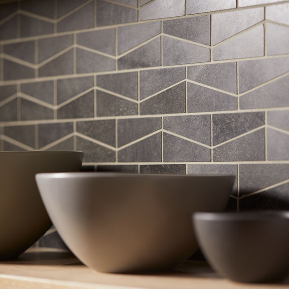 Kitchen backsplash with dark grey wedge-shaped mosaic tile. Three bowls on the countertop.