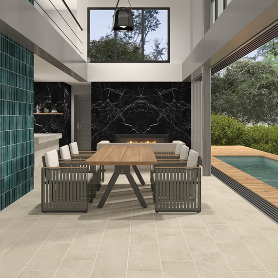Dining room with beige stone look floor tile, aqua wall tile, black marble look porcelain fireplace surround, table & chairs, bifold glass doors open to backyard pool. 