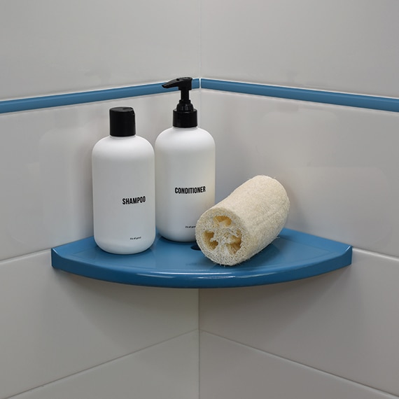 Closeup of blue shower shelf holding bottles and loofah, white wall tile with blue jolly trim.