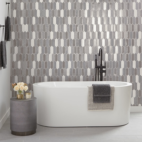 Bathroom with soaking tub, black faucet, white marble & gray limestone picket mosaic backsplash, and gray marble floor tile.