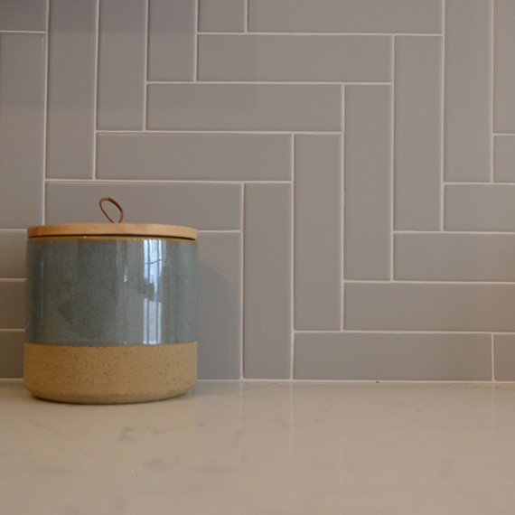 Closeup of kitchen white quartz countertop and gray wall tile in a herringbone pattern.