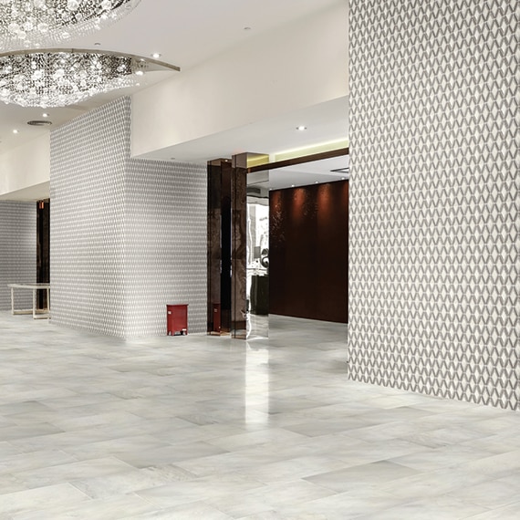 Hotel lobby with white marble floor tile, white & gray marble diamond-shaped mosaic wall tile, and large crystal chandeliers.