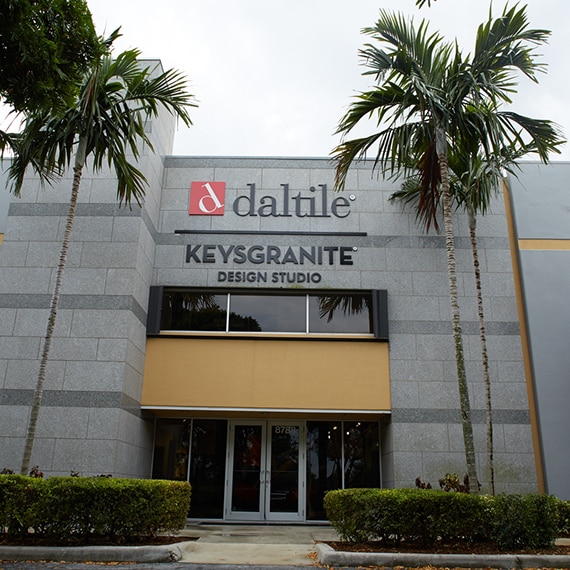 Store front of Daltile Design Studio with gray stone façade and three palm trees.