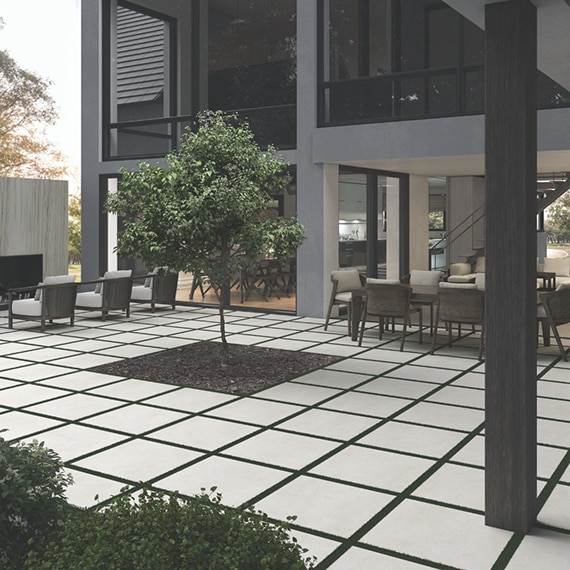 Courtyard of two-story house with dining table & chairs, outdoor fireplace & seating area, and tree in the middle of white 2CM pavers.