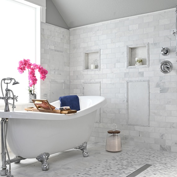 Bathroom with gray marble wall tile and floor tile, free-standing claw-foot bathtub in wet room with two shower niches.