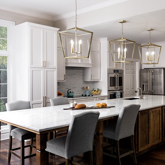 Renovated kitchen with white cabinets, stainless steel appliances, white & gray marble backsplash, countertops, and brass cage pendants over island.