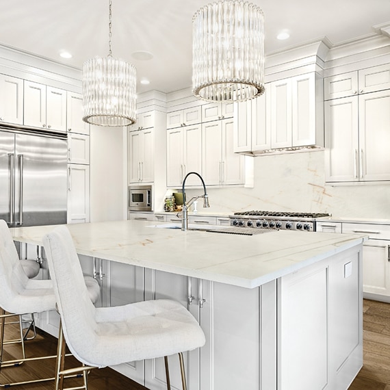 Eat-in kitchen with pendant lighting, white & tan quartzite counters, island with built in sink, white cabinets, stainless steel gas stove and refrigerator.
