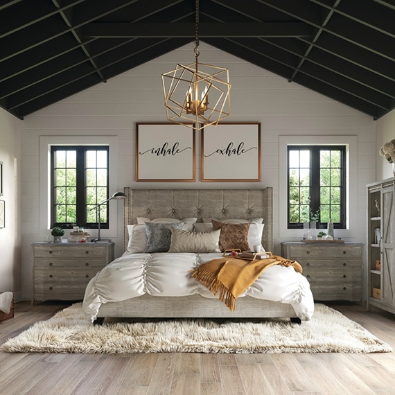 Modern farmhouse bedroom with floor tile that looks like wood, beige fuzzy rug under bed, gray wood furniture, and copper cage pendant.