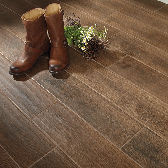 Closeup of mudroom floor of porcelain tile flooring that looks like wood planks and leather cowboy boots next to a bundle of wild flowers.