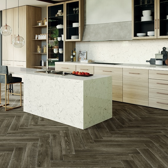 Kitchen with herringbone floor tile that looks like wood, off-white quartz with gray veining on island, countertops, and backsplash, and wood cabinets with open shelves. 